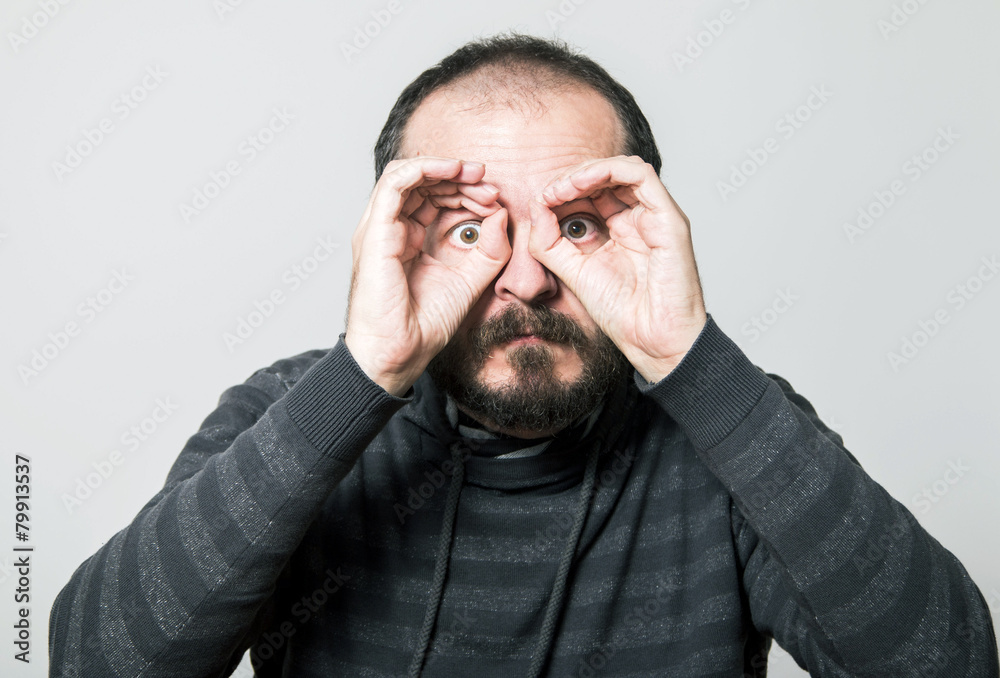 Shocked man looking through hands, making binoculars