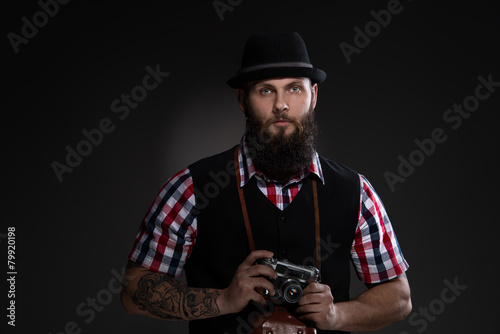 Bearded man in a hat holding an old camera