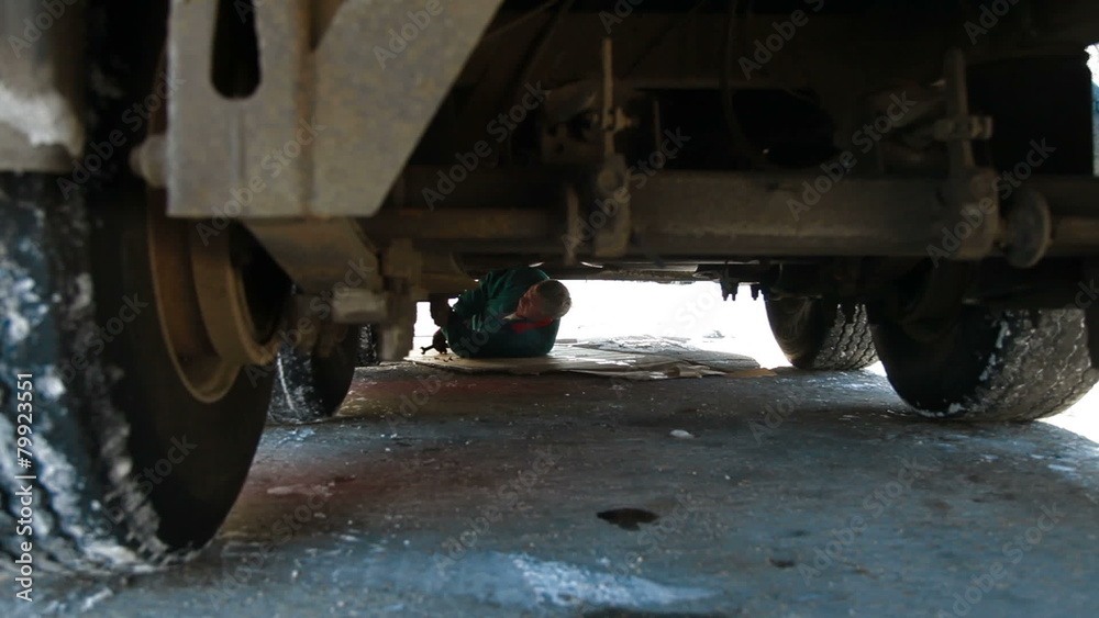 truck driver makes repair lying on road under  vehicle in winter