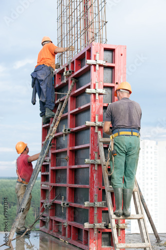 Construction workers mounting concrete formwork with crane