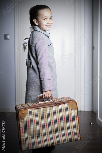 Niña sonriente con maleta vintage en la mano