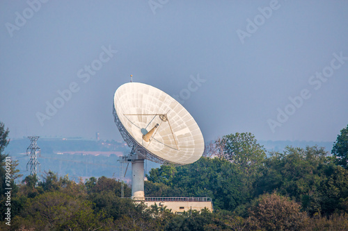 Large satellite dish on the forest over clouded background