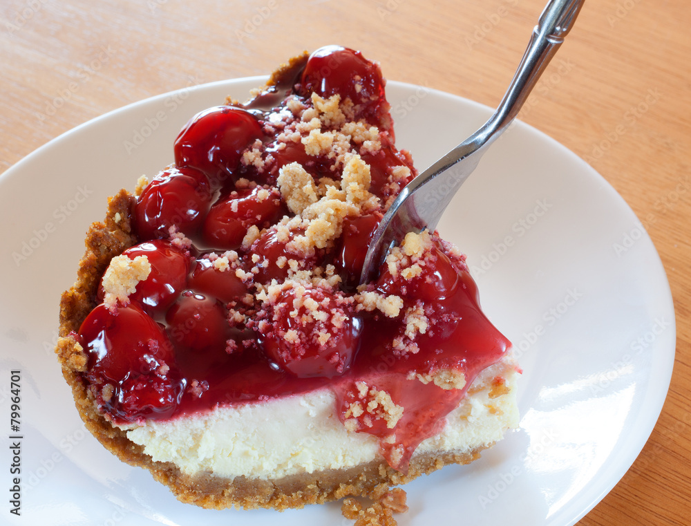 First bite of cherry covered cheesecake coming off the serving First bite of cherry covered cheesecake coming off the serving