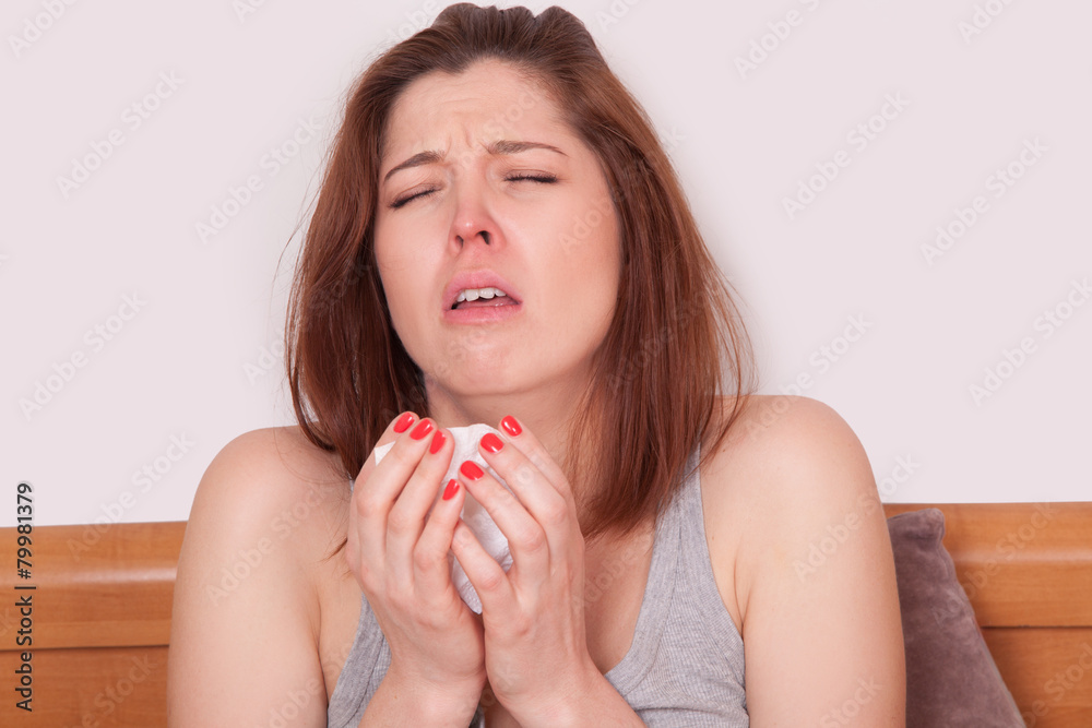 Young sick woman with red nose sitting in bed and sneezing. Young sick woman with red nose sitting in bed and sneezing.