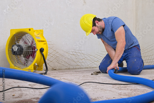 Worker fixing hose of dehumidifier in an apartment which is damaged by flooding photo
