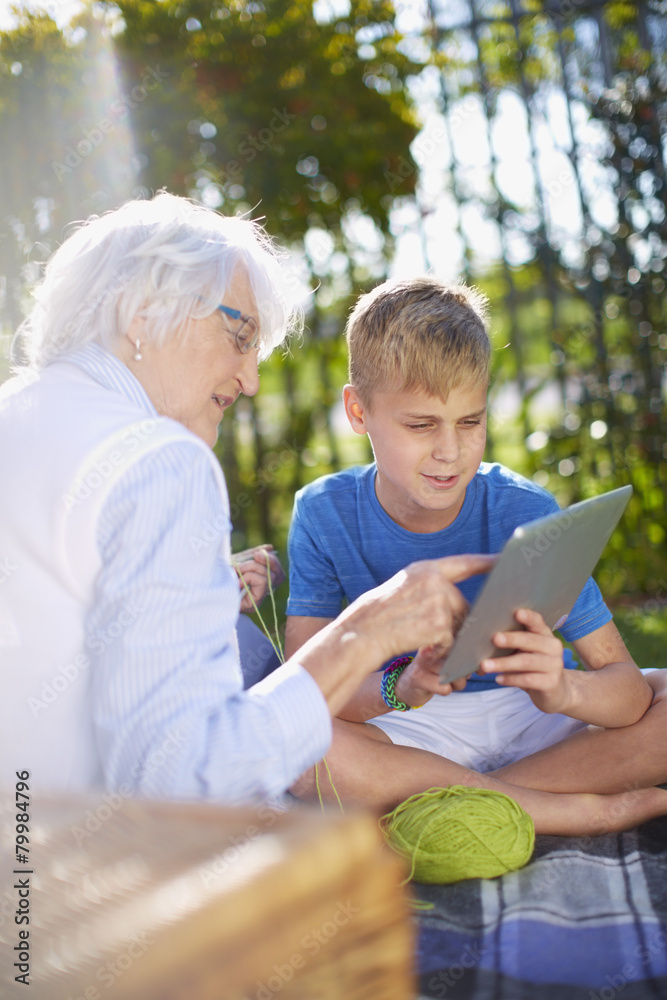 Grandson with digital tablet and grandmother on picnic blanket Grandson with digital tablet and grandmother on picnic blanket