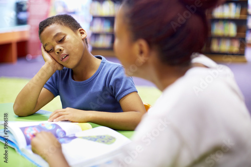 Young teacher and reluctant boy at table photo