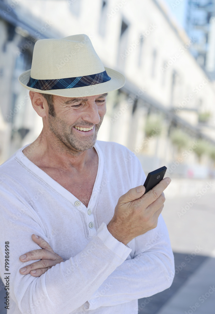 Portrait of smiling mature man with stubble and summer hat using smartphone Portrait of smiling mature man with stubble and summer hat using smartphone