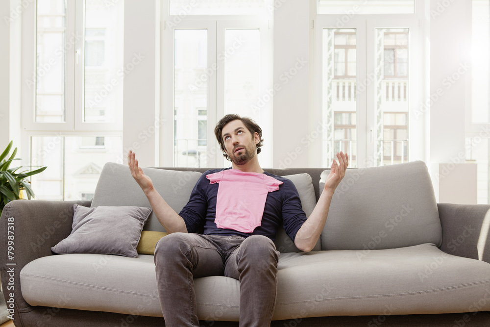 Disappointed man with pink baby shirt on couch Disappointed man with pink baby shirt on couch