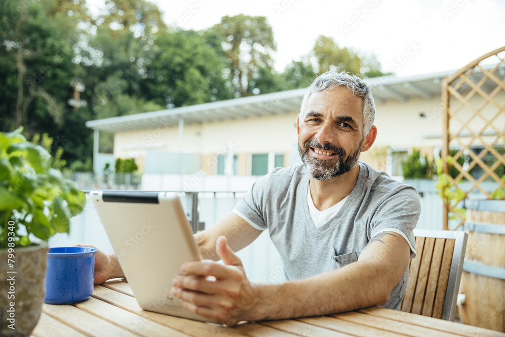 Portrait of smiling man sitting on his balcony using digital tablet Portrait of smiling man sitting on his balcony using digital tablet
