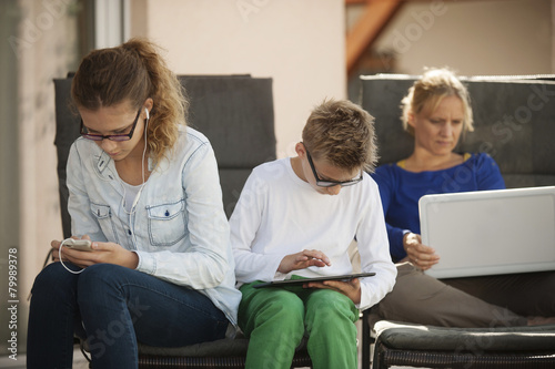 Mother and her two children relaxing with digital tablet, smartphone and laptop on the terrace photo