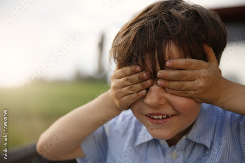 Portrait of smiling little boy covering eyes with his hands