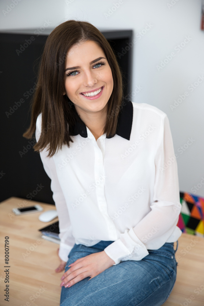 Cheerful young businesswoman sitting on the table in office Cheerful young businesswoman sitting on the table in office