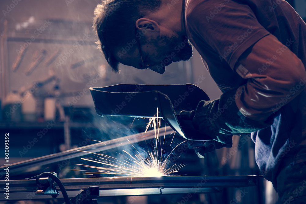 Employee at the factory welding steel using MIG MAG welder. - obrazy, fototapety, plakaty 