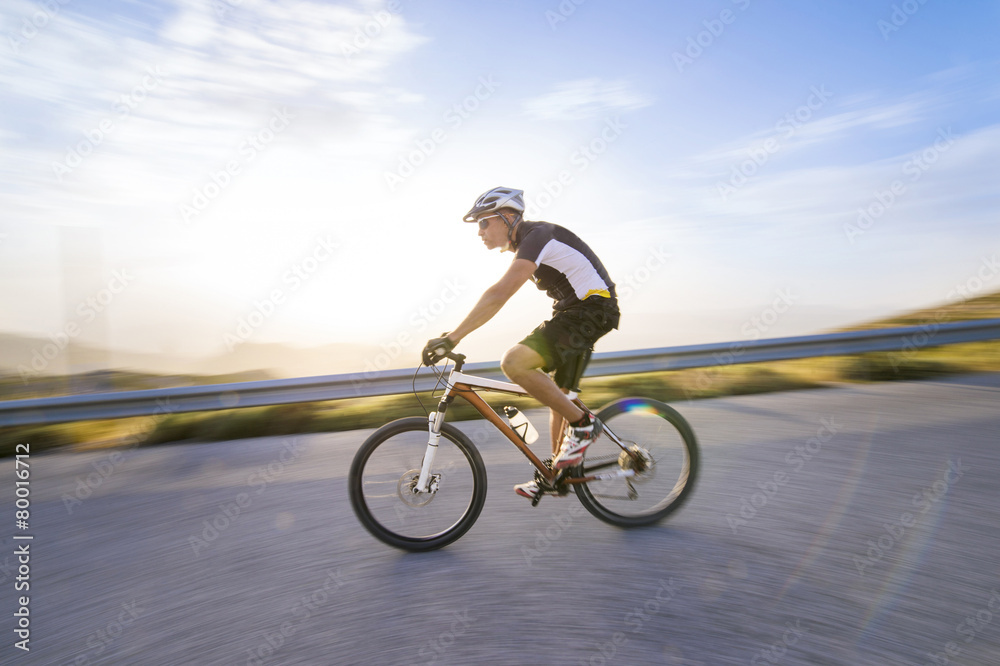 Cyclist man riding mountain bike in sunny day on a mountain road Cyclist man riding mountain bike in sunny day on a mountain road