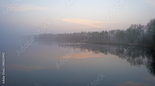 The shore of a foggy lake in winter at dawn