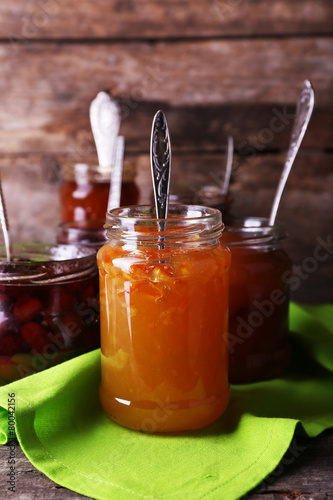 Jars of tasty jam with napkin on wooden background