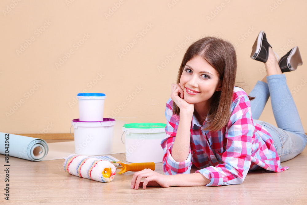 Beautiful girl lying on floor with equipment for painting wall Beautiful girl lying on floor with equipment for painting wall