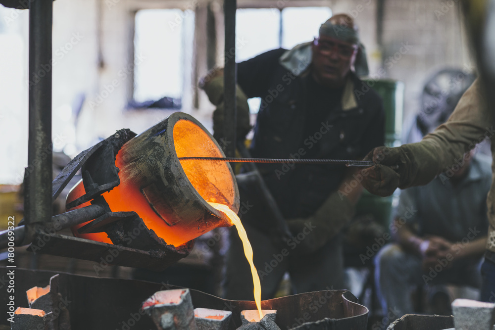 Closeup of hands racking melted bronze into molds using a crucib Stock