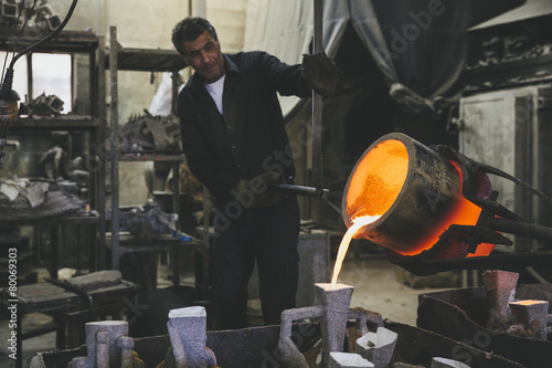 Middle aged man pouring melted bronze into molds using a crucibl