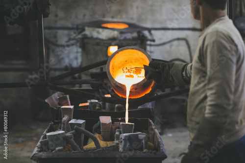 Man pouring melted bronze into molds using a crucible photo