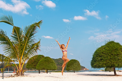 Happy woman jumping at the beach against blue sky and palm photo