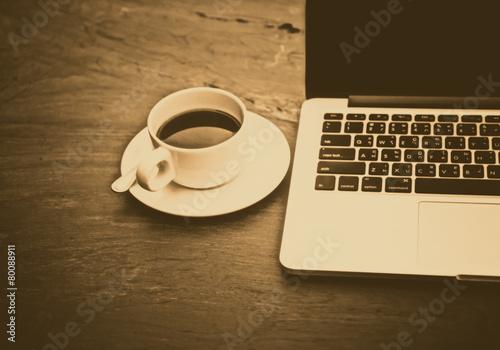 Black coffee in a white cup on a table with a computer.