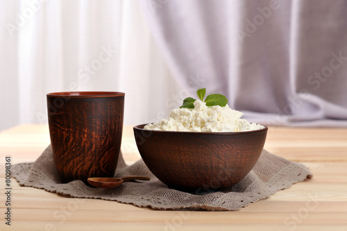 Cottage cheese in bowl with cup on table on fabric background