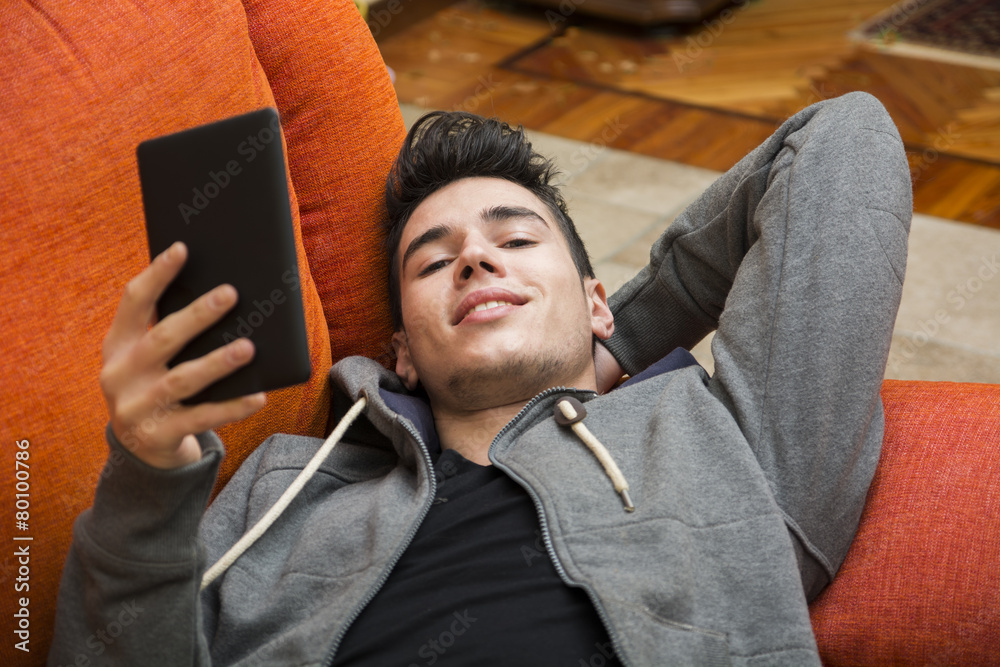 Handsome young man at home reading with ebook reader Handsome young man at home reading with ebook reader