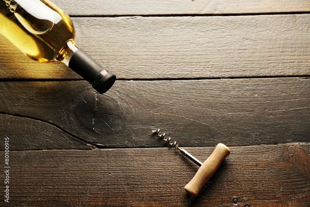 Glass bottle of wine with corkscrew on wooden table background