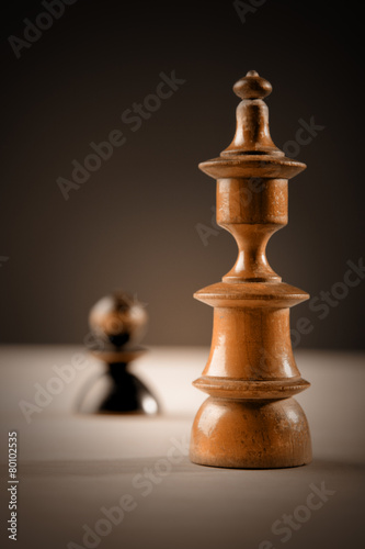Chess. Black pawn and white king on wooden table.