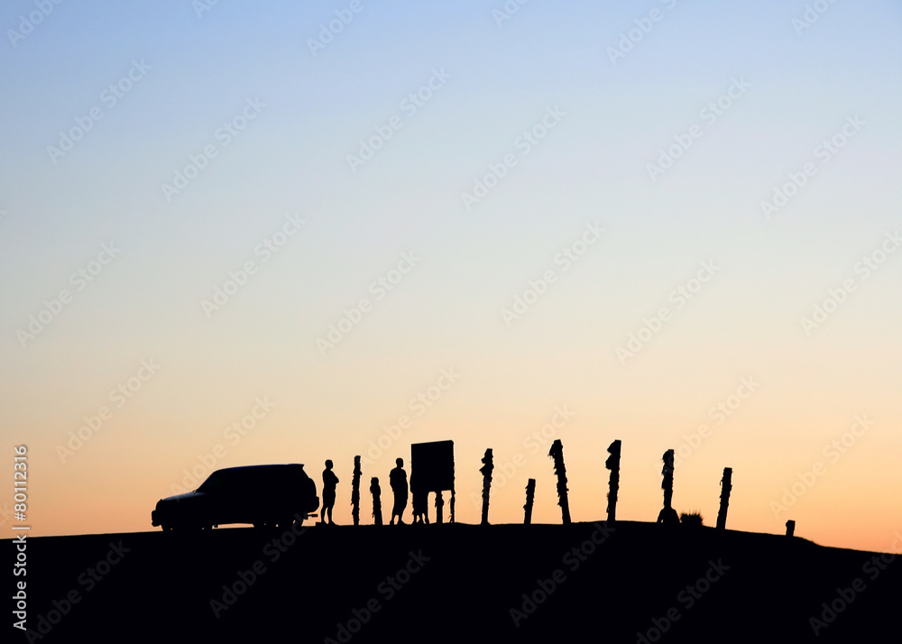 Silhouettes of a car and people on the sky background