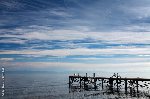 Dock with people and bike on the blue sky background