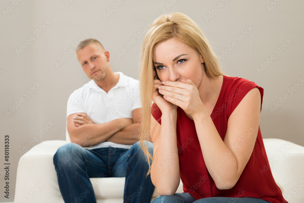 Wife Talking On Mobile Phone While Husband On Sofa Wife Talking On Mobile Phone While Husband On Sofa