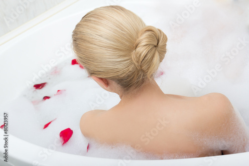 back view of woman relaxing in bath with red flower petals