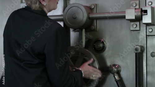Woman opens a large bank vault door.  Close up.