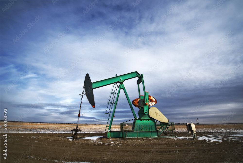 An oil pump jack at a drilling site for oil, an oil field in Saskatchewan. An oil pump jack at a drilling site for oil, an oil field in Saskatchewan.