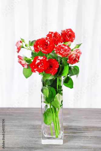 Beautiful roses in vase on table on light background © Africa Studio