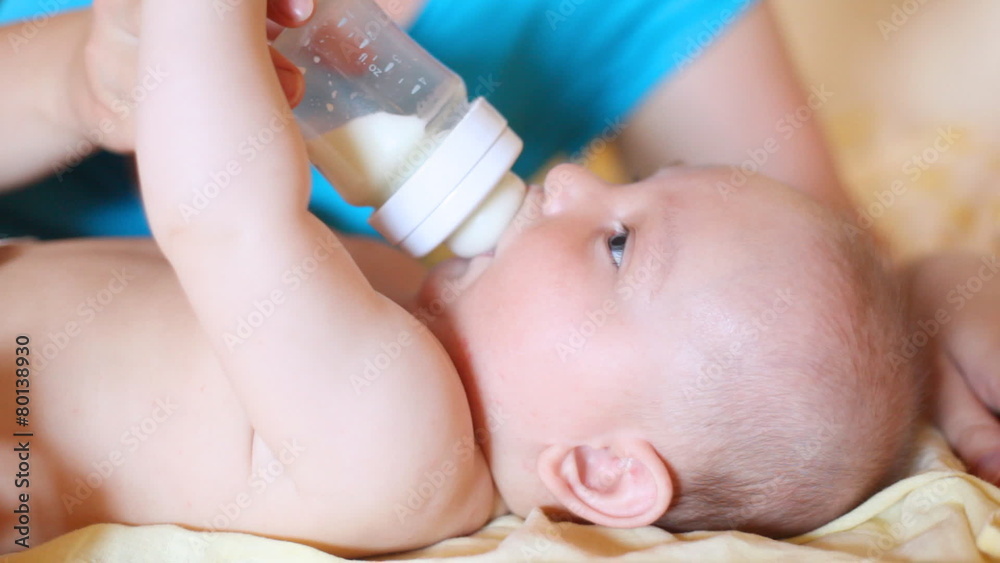small child drinks milk from small bottle in hands of mother lying on back small child drinks milk from small bottle in hands of mother lying on back