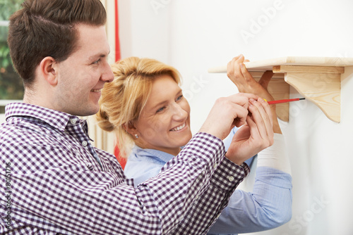 Couple Putting Up Wooden Shelf Together At Home photo