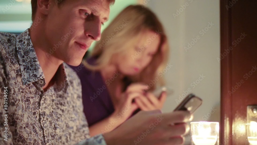 couple sitting in restaurant with candles and looking to phones couple sitting in restaurant with candles and looking to phones
