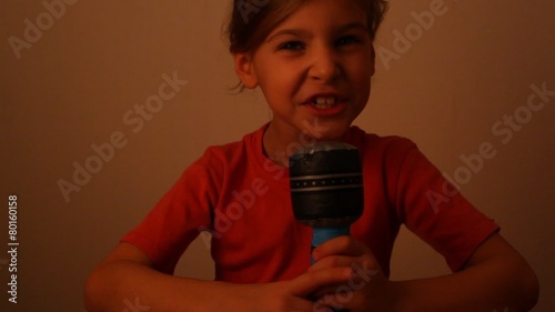 Cute little girl talking on microphone toy while lights are turned off, isolated on white photo