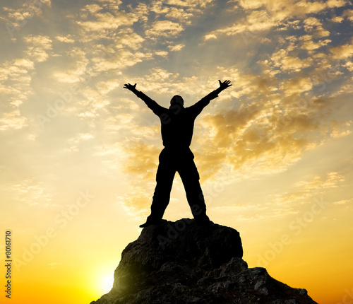 Silhouette of the person standing on a rock in beams of a declin