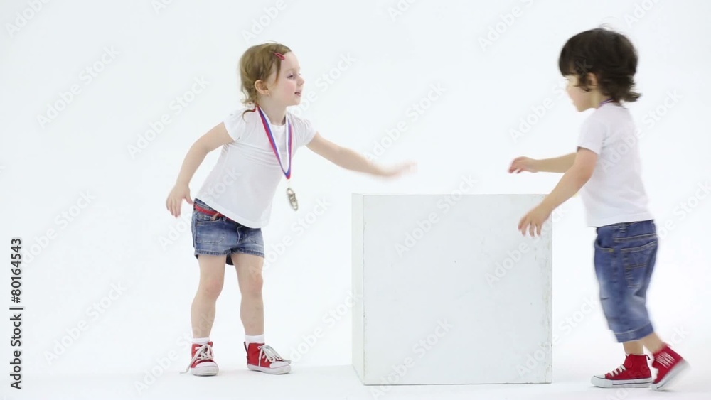 Little girl and boy in shorts with medal plays with big cube
