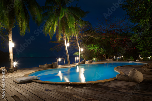Swimming pool with palms on beach at night