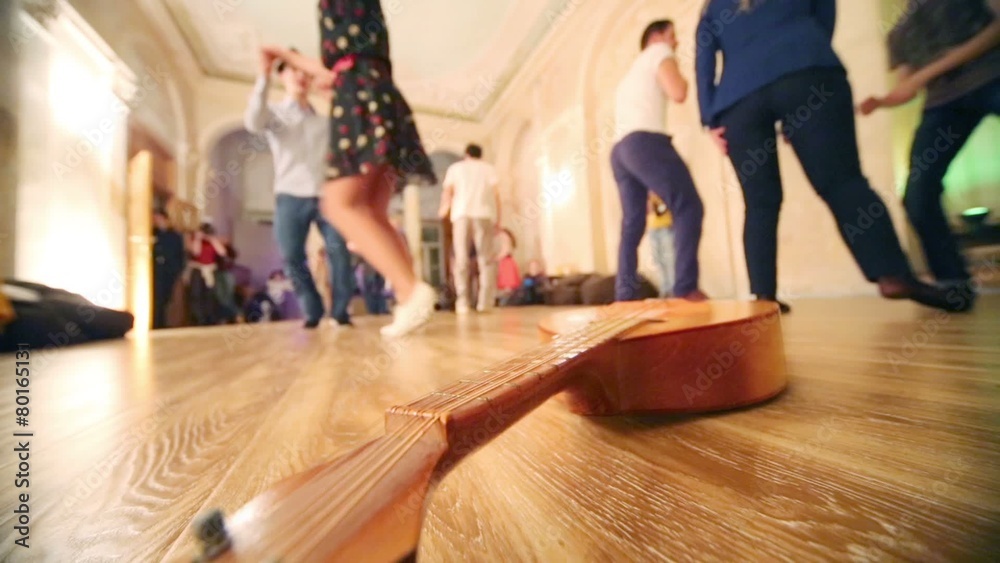Wooden guitar lies on floor and young people dance in hall Wooden guitar lies on floor and young people dance in hall
