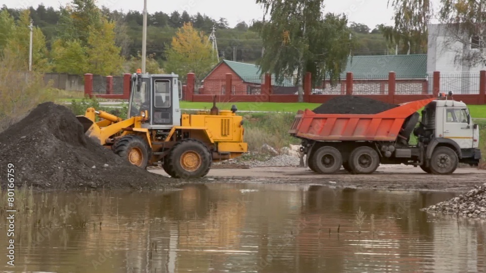 Loader takes ground from pile for load truck near country house Loader takes ground from pile for load truck near country house