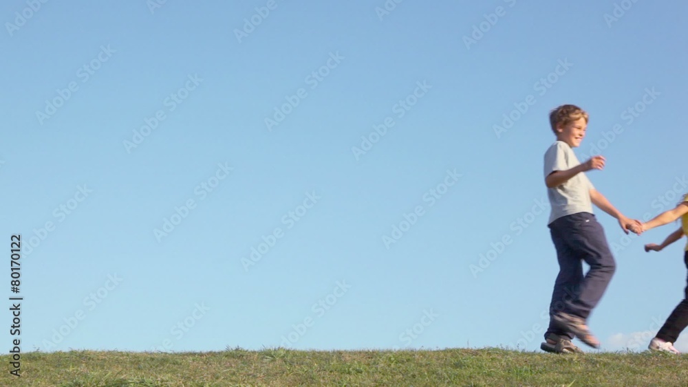 Children boy with little girl hold hands and walk by grass hill at sunny summer day Children boy with little girl hold hands and walk by grass hill at sunny summer day
