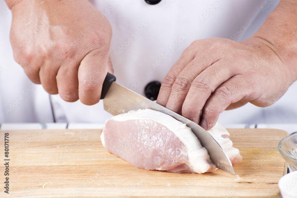 Chef cutting raw pork on wooden board