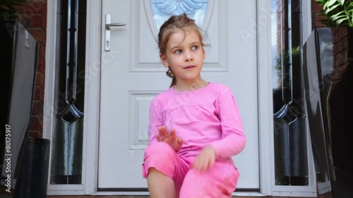 Little girl plays when sits alone on porch near door of cottage